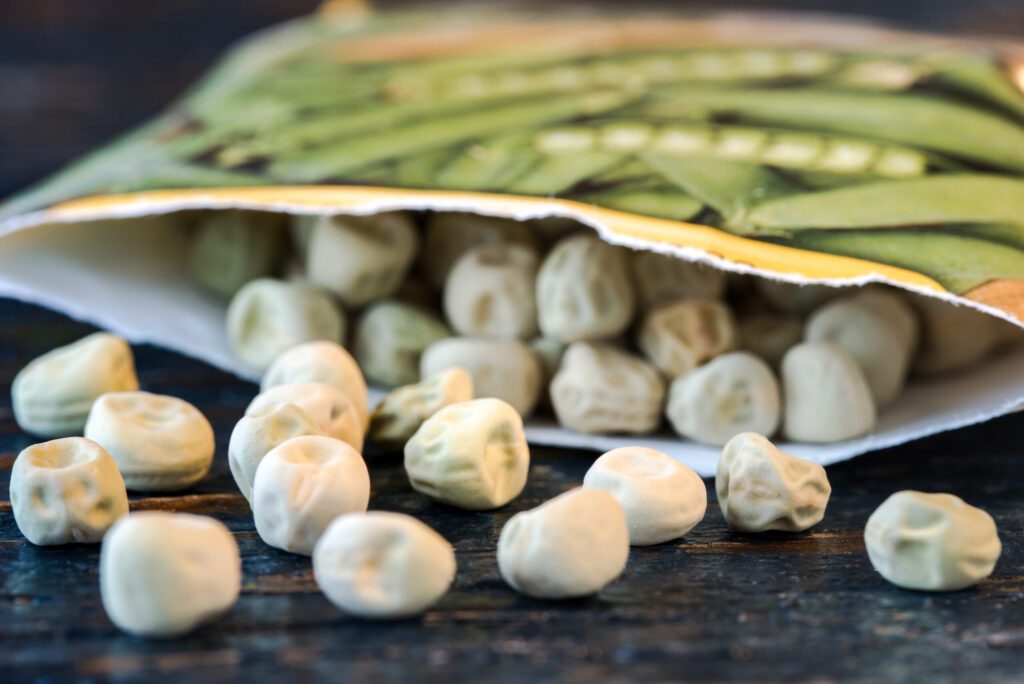 Garden peas spill out of a seed packet onto a table | City Floral Garden Center - Denver